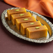 Rectangular Badam Mysore pak sweet placed on a silver platter with an orange cloth in the background.